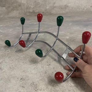 May include: A chrome coat rack with five hooks. The hooks are finished with red and green teardrop-shaped caps.