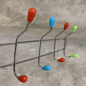 Può includere: Un appendiabiti cromato con sei ganci. I ganci hanno punte di plastica colorate in rosso, blu e verde.