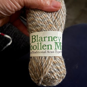 Könnte beinhalten: Eine Garnrolle von Blarney Woolen Mills in einer braunen, beige und weißen Farbkombination. Das Etikett lautet "Blarney Woolen Mills" und "True to Traditional Aran Type Pattern".