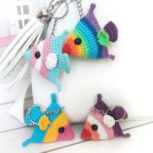 Könnte beinhalten: Vier gehäkelte Fisch-Schlüsselanhänger in verschiedenen Farbkombinationen. Die Fische sind Regenbogen, rosa und blau, gelb und rosa sowie lila und rosa. Die Schlüsselanhänger sind an silbernen Schlüsselringen befestigt.