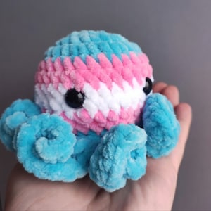 May include: A crocheted octopus plush toy with blue tentacles and a head with pink, white, and blue stripes. The octopus has black eyes.