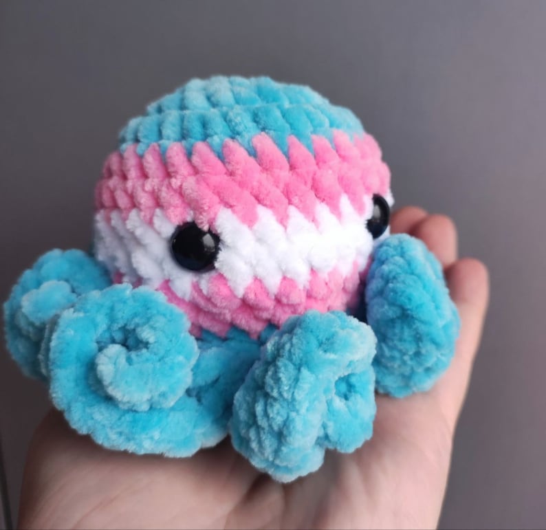 May include: A crocheted octopus plush toy with blue tentacles and a head with pink, white, and blue stripes. The octopus has black eyes.
