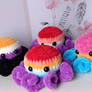 Könnte beinhalten: Drei gehäkelte Octopus-Plüschtiere in verschiedenen Farbkombinationen. Der erste Octopus ist orange, weiß und lila mit schwarzen Tentakeln. Der zweite Octopus ist rot, orange, gelb und weiß mit lila Tentakeln. Der dritte Octopus ist pink mit orangefarbenen und gelben Akzenten und blauen Tentakeln.