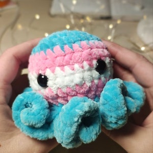 May include: A crocheted octopus plush toy with a blue and pink color scheme. The octopus has a white face with black eyes.
