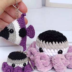 May include: Two crocheted octopus keychains in purple, white, grey, and black colours. The larger octopus has a fluffy texture. The smaller octopus is made with a smooth yarn.