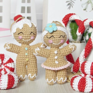 May include: Two crocheted gingerbread people ornaments, one with a blue flower and the other with a red hat, standing next to two red and white candy cane ornaments.