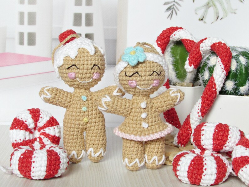May include: Two crocheted gingerbread people ornaments, one with a blue flower and the other with a red hat, standing next to two red and white candy cane ornaments.