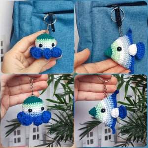Op de afbeelding: Twee gebreide sleutelhangers, een in de vorm van een octopus en de andere in de vorm van een vis. Beide zijn in tinten groen, wit en blauw, met witte ogen en een witte cirkel op de vis. De sleutelhangers zijn bevestigd aan zilveren sleutelringen.