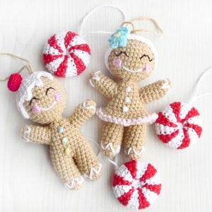 May include: Three crocheted gingerbread ornaments, two are gingerbread people and one is a peppermint candy. The gingerbread people have white icing and smiling faces. The peppermint candy is red and white.