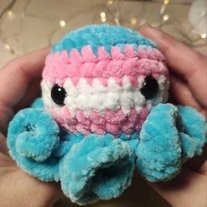 May include: A crocheted octopus plush toy with blue, pink, and white yarn. The octopus has large black eyes and a curled tentacle.