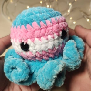 May include: A crocheted octopus plush toy with blue, pink, and white yarn, resembling the transgender pride flag.