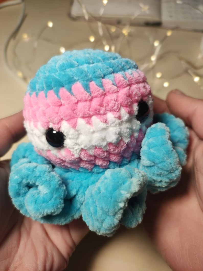 May include: A crocheted octopus plush toy with blue, pink, and white yarn, resembling the transgender pride flag.