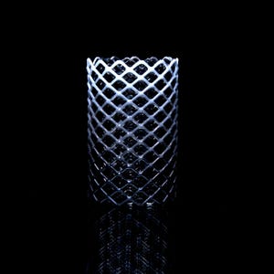 May include: A cylindrical object with a diamond-shaped lattice design. The object is white and appears to be made of a rigid material. The background is black, and the object's reflection is visible below.