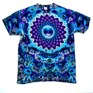 May include: A short-sleeve t-shirt featuring a tie-dye pattern in shades of deep purple, bright blue, and black. The center of the chest displays a large, symmetrical, multi-layered mandala graphic in vibrant purple and blue tones.