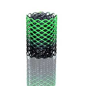 May include: A cylindrical, open-weave object with a gradient of green to black. The diamond-shaped mesh is tightly woven, creating a textured surface. The object is set against a white background, with a slight reflection.