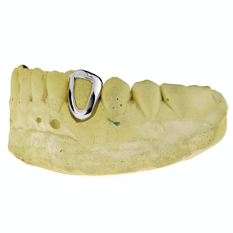 May include: A silver tooth grill with a single, oval-shaped piece. The grill is displayed on a model of a mouth.