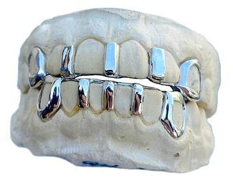 May include: Silver grillz for teeth, with a design that includes a single large tooth and several smaller teeth. The grillz are shown on a white mold of a mouth.