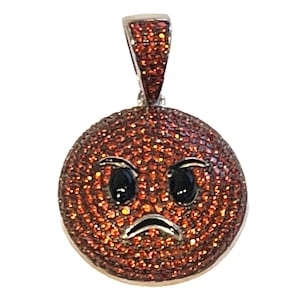 May include: A silver pendant with a red, angry emoji face made of small red crystals. The emoji has black eyes and a frowning mouth.
