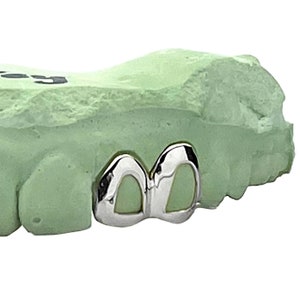 May include: Close-up of a dental model with two silver-colored crowns. The crowns are smooth and shiny, and they are attached to the model with a green material.