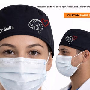 May include: Navy blue scrub cap with an embroidered brain and heart design. The cap has the text "Dr. Smith" and the words "CUSTOM NAME AVAILABLE". The cap is worn by a person wearing a surgical mask.