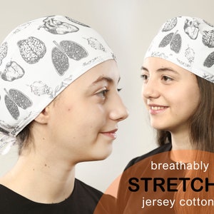 Könnte beinhalten: Zwei Personen tragen weiße OP-Hauben mit einem anatomischen Schwarz-Weiß-Druck. Die Hauben sind aus dehnbarem Jersey-Baumwolle und atmungsaktiv. Der Text "breathably STRETCHY jersey cotton" ist unten im Bild gedruckt.