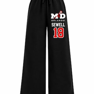 May include: Black wide-leg sweatpants with an elastic drawstring waistband. The right leg features a white and red graphic print with the text M&D, ORLANDO, SEWELL, and the number 18, accompanied by a small red and white lacrosse stick icon.