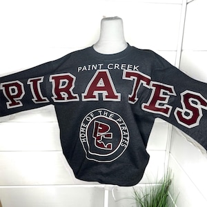 May include: A dark gray long-sleeve sweatshirt featuring the text PAINT CREEK PIRATES in large maroon letters with white outlines. Below the text is a circular logo containing the letters PC and the words HOME OF THE PIRATES in white.