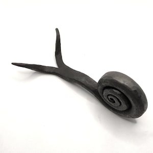 Puede incluir: Una escultura de caracol de metal negro con una cola larga y bifurcada. El caracol está hecho de una sola pieza de metal y tiene un diseño realista y detallado.