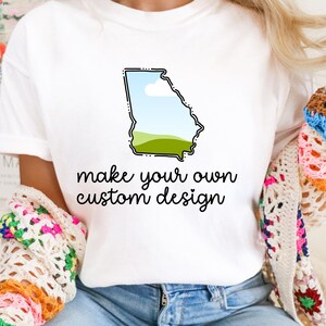 May include: White t-shirt featuring a graphic of the state of Georgia with a landscape design. The shirt has the text "make your own custom design" in black script. The shirt is made of a soft material.