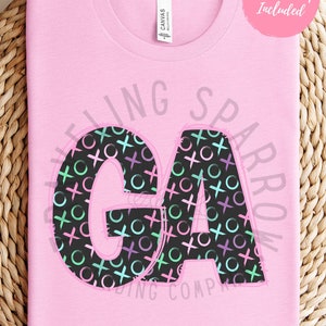 May include: Pink t-shirt featuring a black and white graphic of the letters "GA" with a pattern of circles and crosses in pink, green, and blue.