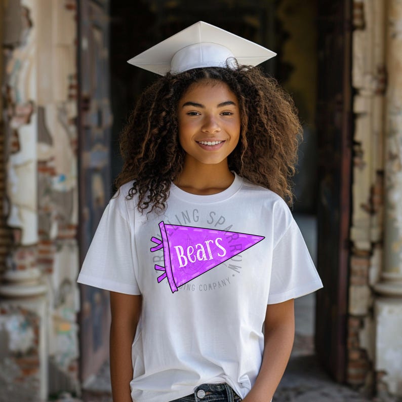 Pode incluir: Uma pessoa vestindo uma camiseta branca com um design de fl&acirc;mula roxa que diz "Bears". A pessoa tamb&eacute;m est&aacute; usando um chap&eacute;u de formatura branco. O fundo &eacute; um ambiente externo desfocado.