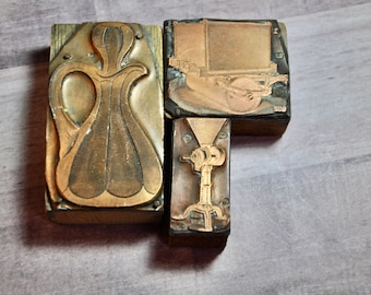 Op de afbeelding: Drie vintage houten drukblokken met metalen letters. De blokken tonen een kan, een wagen en een klein apparaat.