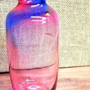 May include: A cylindrical glass vase featuring a gradient color transition from a deep blue rim down to a vibrant pink base. The glass is translucent, allowing light to pass through the vessel, which has a smooth, rounded neck and a wide opening.