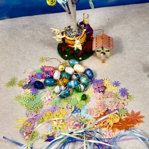 以下が含まれることがあります： パステルカラーのウサギのツリー、バードハウス、パステルカラーの卵、さまざまなパステルカラーのペーパーフラワーとリボンなど、イースターの装飾品のコレクションです。