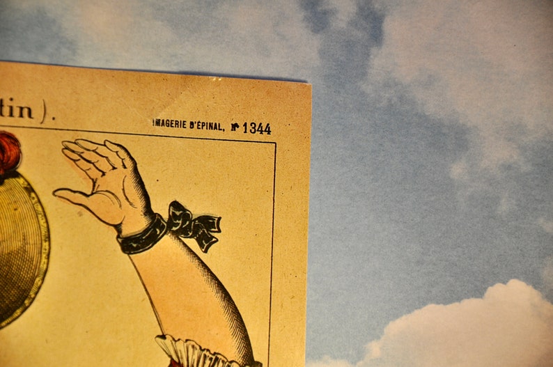 May include: A vintage paper print featuring a detailed illustration of an arm with a dark wristband and a bow, positioned next to the text IMAGERIE D'&Eacute;PINAL, N 1344. The print has a beige background and is set against a blue sky with white clouds.