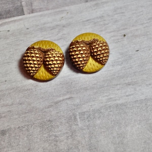 May include: Two brown and gold pinecone buttons. The buttons are round and have a textured surface.