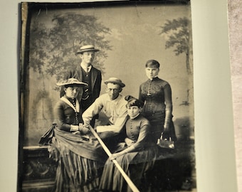 May include: A black and white vintage photograph of five people posing for a portrait.  The group is standing in front of a backdrop of trees.  Three of the people are wearing hats.  One person is holding a long, thin object.