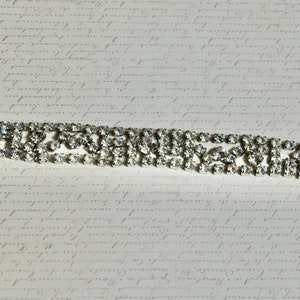 May include: A silver rhinestone bracelet with a geometric design. The bracelet is made of multiple rows of rhinestones.