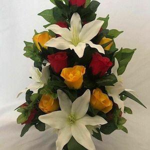 May include: An artificial flower arrangement featuring white and yellow flowers, including red roses and white lilies. The arrangement is in a green vase and is set against a white background.