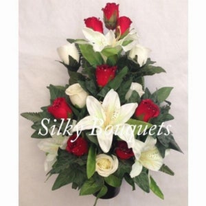 May include: A white and red artificial flower arrangement in a black vase. The arrangement features white lilies, white roses, and red roses. The text "Silky Bouquets" is visible in the image.
