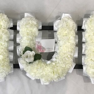 May include: White floral arrangement spelling out the word "MOM" with white lilies and white ribbon accents.