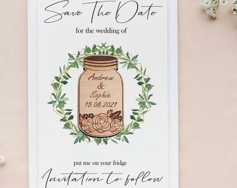 May include: A wedding invitation card with the text "Save The Date" and "Invitation to follow". The card features a wooden jar design with the names "Andrew & Sophie" and the date "15.08.2021", surrounded by a green wreath.