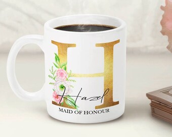 May include: White ceramic mug with a gold letter H and floral design. The mug says "Hazel Maid of Honour".