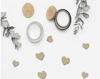 May include: A white wooden surface with two candles, two cork circles, and several small wooden hearts scattered across the surface. The candles are in glass jars with white wax. The hearts are in various shades of brown.