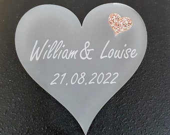 May include: A white frosted heart-shaped plaque with the text "William & Louise 21.08.2022" and a small pink glitter heart.