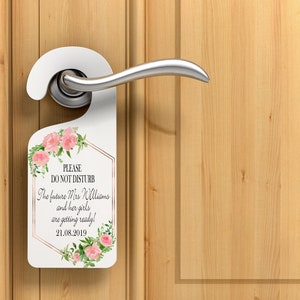 Puede incluir: Colgador de puerta blanco con detalles florales y el texto "PLEASE DO NOT DISTURB". El texto contin&uacute;a con "The future Mrs Williams and her girls are getting ready! 21.08.2019". El colgador est&aacute; en una manija de puerta y una puerta de madera.