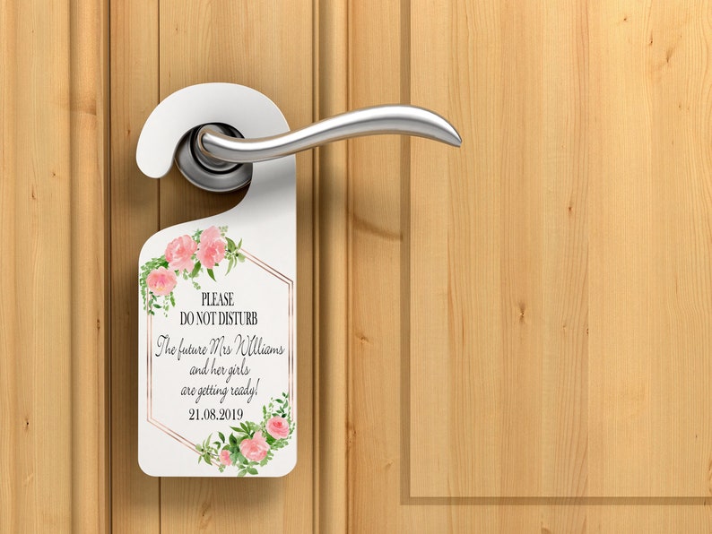 Puede incluir: Colgador de puerta blanco con detalles florales y el texto "PLEASE DO NOT DISTURB". El texto contin&uacute;a con "The future Mrs Williams and her girls are getting ready! 21.08.2019". El colgador est&aacute; en una manija de puerta y una puerta de madera.