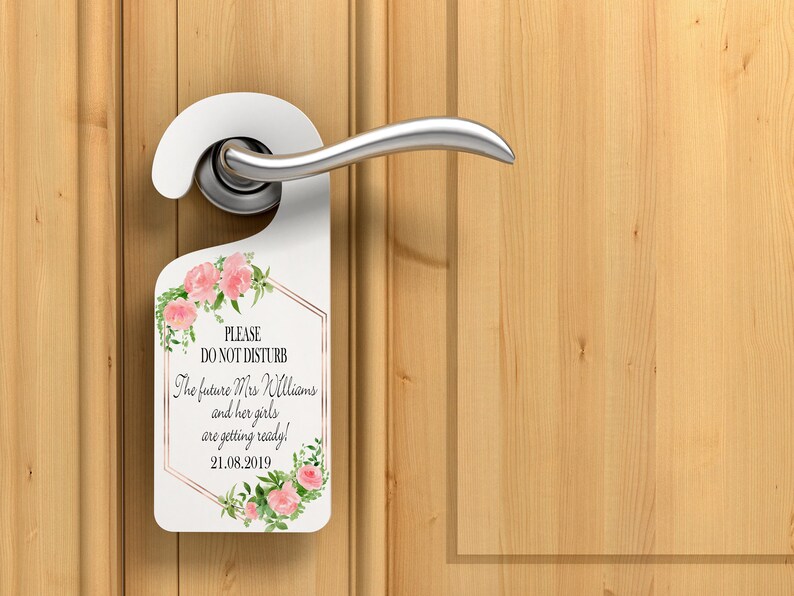 Puede incluir: Colgador de puerta blanco con detalles florales y el texto "PLEASE DO NOT DISTURB". El texto contin&uacute;a con "The future Mrs Williams and her girls are getting ready! 21.08.2019". El colgador est&aacute; en una manija de puerta y una puerta de madera.
