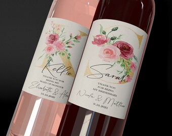 May include: Two wine bottles with personalized labels featuring floral designs and gold lettering. The labels say "Kellie" and "Sarah" with thank you messages for being a maid of honor and bridesmaid. The dates of the weddings are also included.