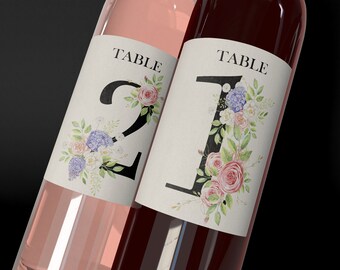 May include: Two wine bottles with labels that say "Table 1" and "Table 2". The labels feature watercolor floral designs in shades of pink, white, and blue.